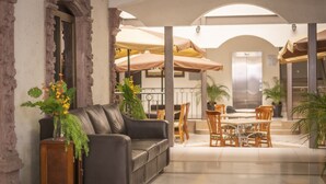 A spacious indoor area with a leather sofa, wooden chairs, and tables under large umbrellas.