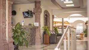 A lobby with a reception desk, potted plants, a clock, and a seating area with umbrellas.