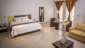 A modern hotel room with a large bed, a chair, a small table, and a vase of flowers.