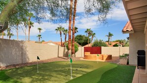A backyard with artificial grass, a putting green, and a red play structure. - Windrose (Scottsdale)