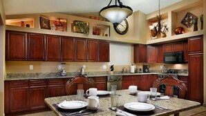 A kitchen with wooden cabinets, granite countertops, a dining table set with plates and cups, and a clock on the wall. - Windrose (Scottsdale)