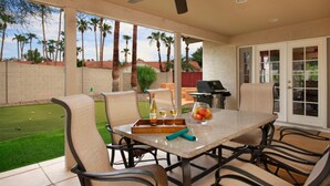 A patio with a table, chairs, a ceiling fan, and a view of a golf course. - Windrose (Scottsdale)