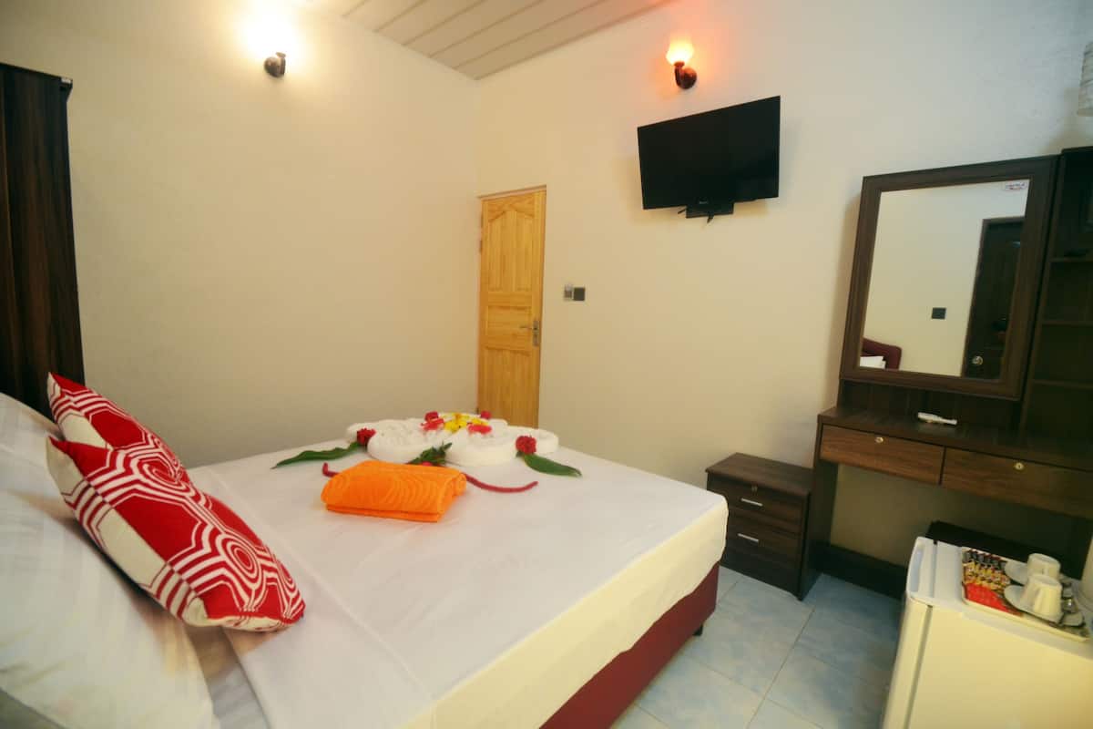 A hotel room with a bed, a TV mounted on the wall, a wooden door, a dresser, and a mirror.