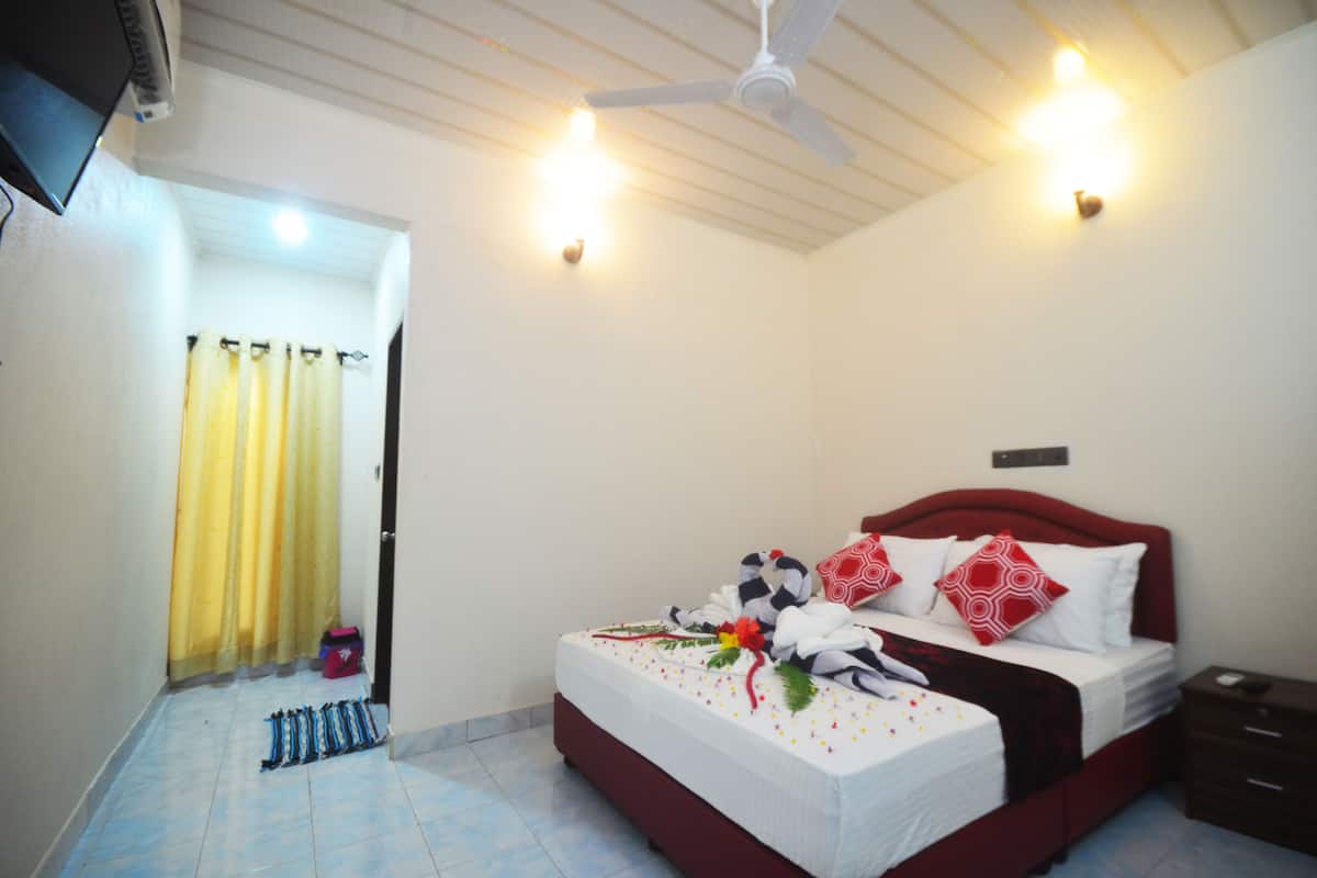 A hotel room with a bed, a bedside table, a ceiling fan, and a window with curtains.