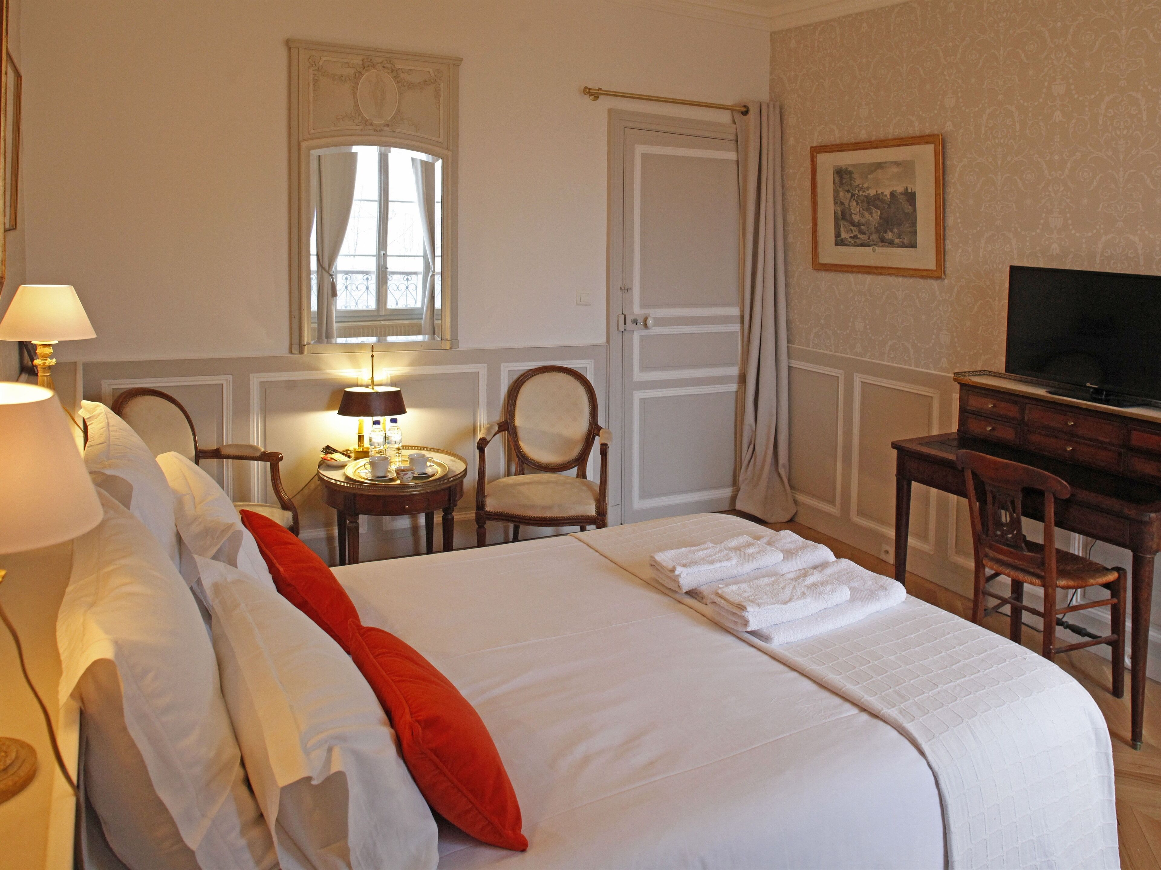 A hotel room with a large bed, a desk, a chair, a television, and a window with curtains.