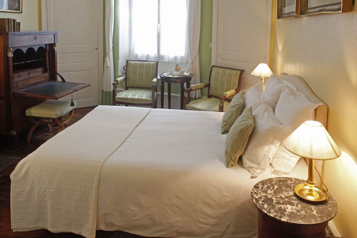 Una habitación de hotel con una cama grande, dos sillas, una mesita y un escritorio con una lámpara.
