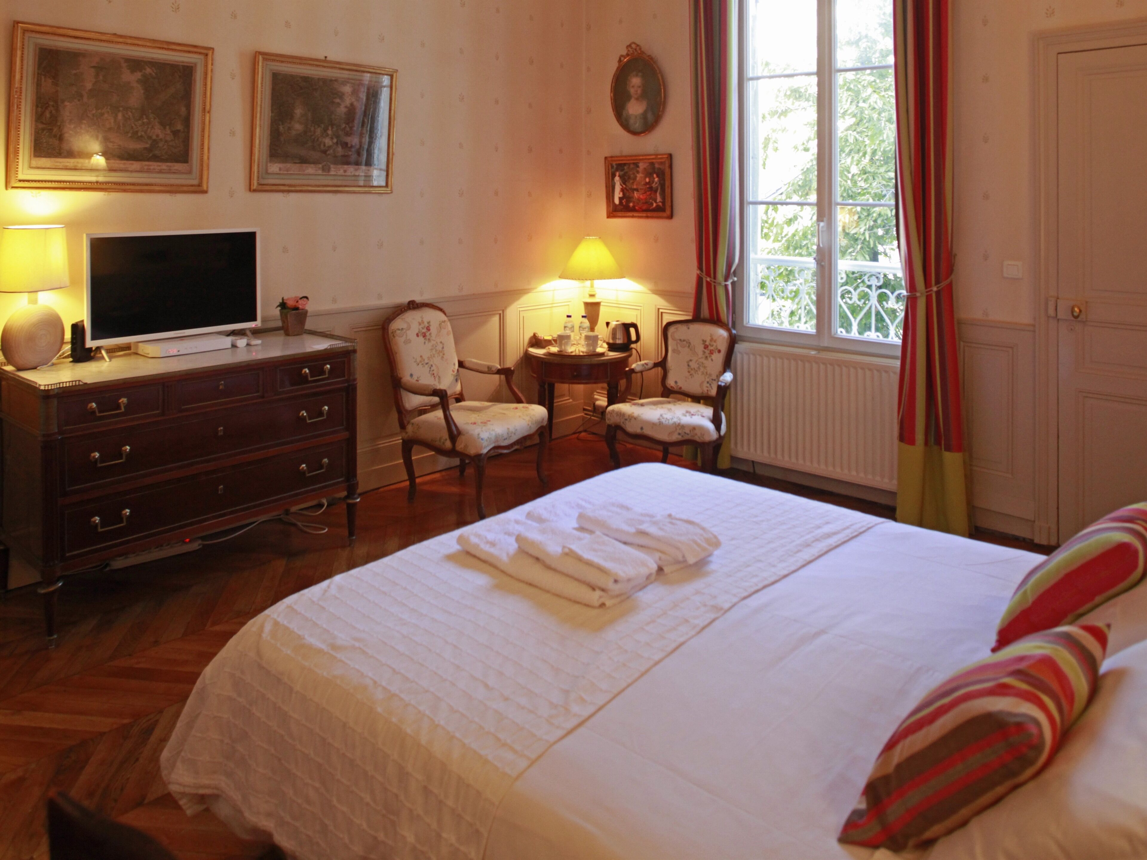 A hotel room with a bed, two armchairs, a desk with a television, and a window with curtains.