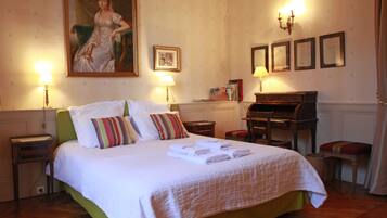 Een hotelkamer met een groot bed, twee nachtkastjes, een bureau, een stoel, een piano en een schilderij aan de muur.
