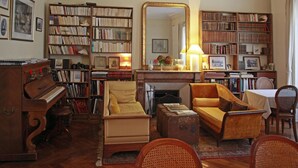 A cozy living room with a piano, a fireplace, a large mirror, and bookshelves filled with books. - Les Chambres de Mathilde (Angers)