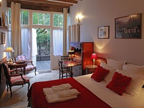 A hotel room with a bed, a desk, a chair, a table, a lamp, and a painting on the wall. - Les Chambres de Mathilde (Angers)
