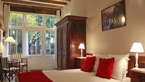 A bedroom with a large bed, two bedside tables with lamps, a wooden wardrobe, and a window with curtains. - Les Chambres de Mathilde (Angers)