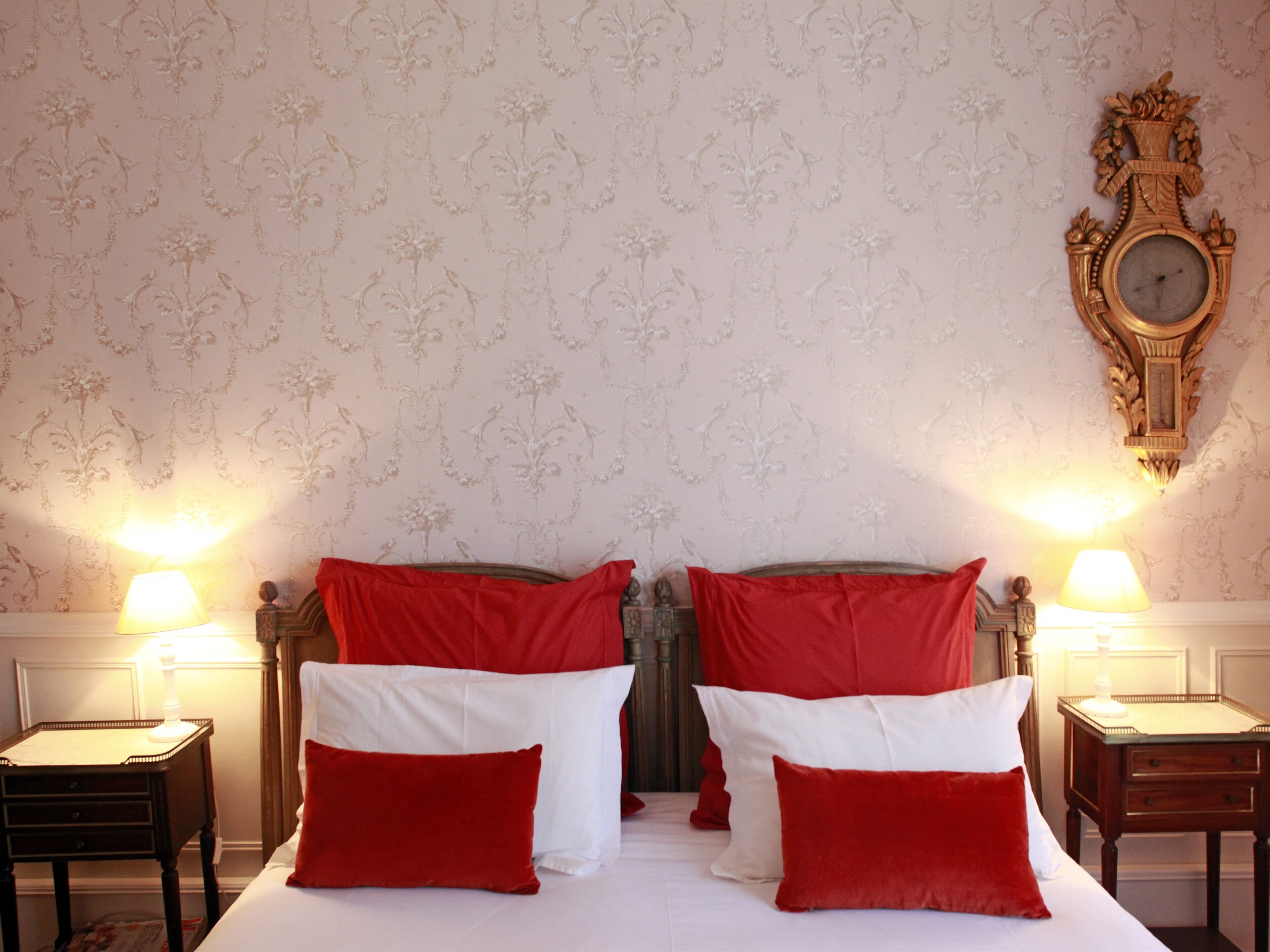 A double bed with red and white pillows, two bedside tables, and a wall clock.