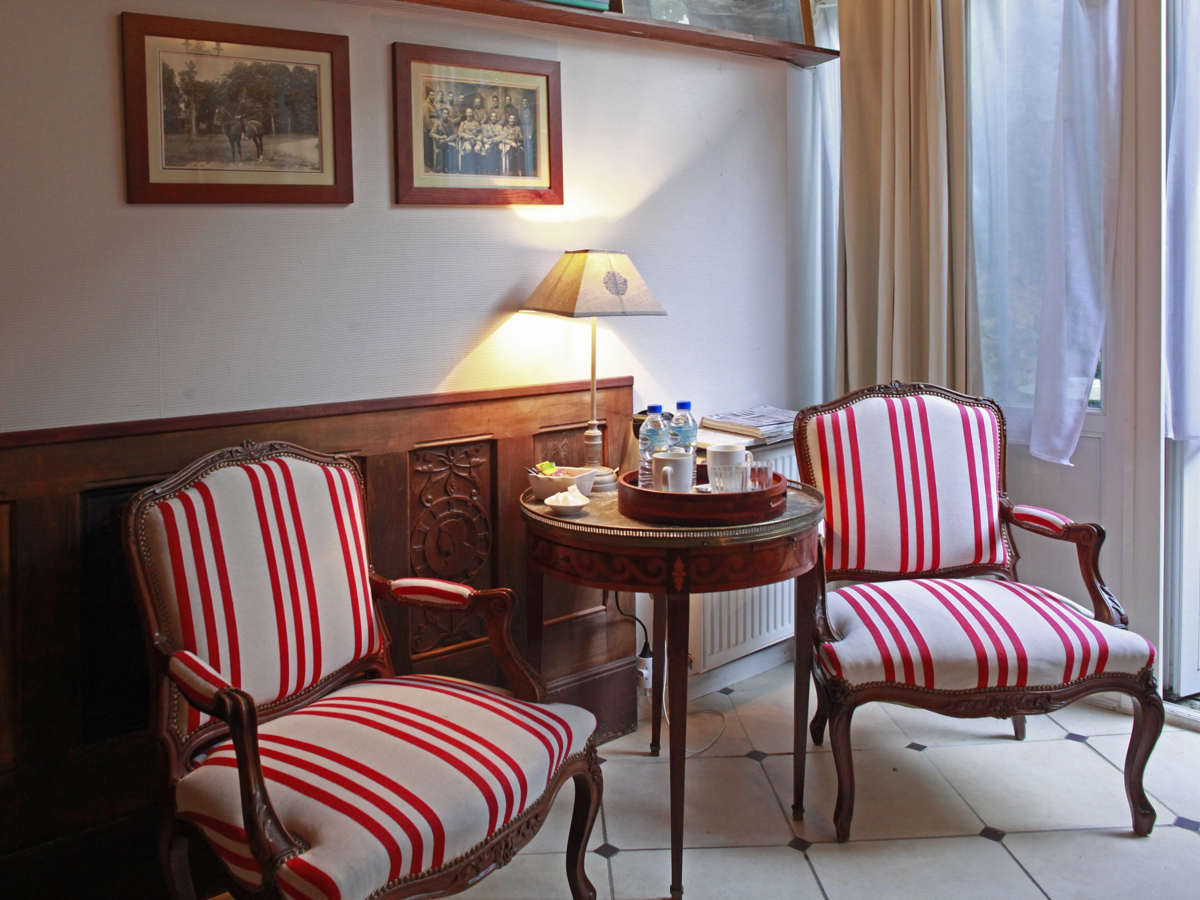 A room with two striped armchairs, a small table with a lamp, and framed pictures on the wall.