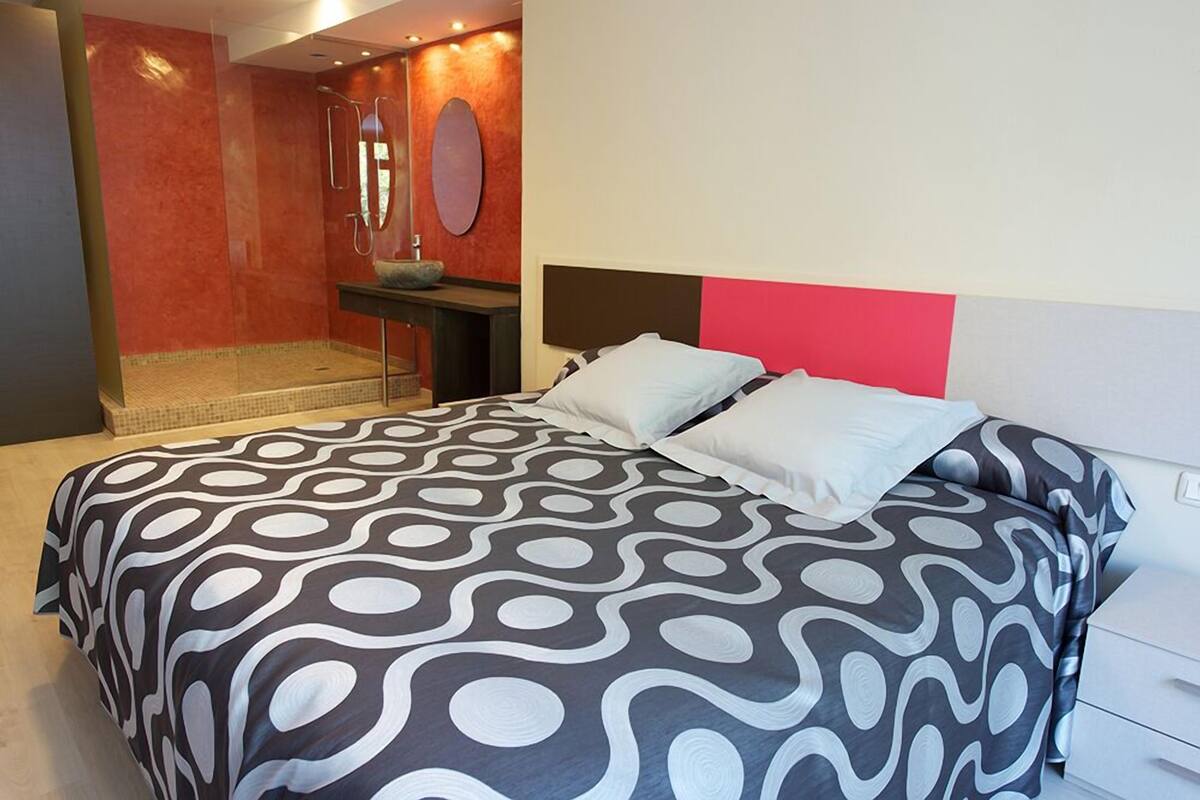 Ein modernes Hotelzimmer mit einem großen Bett, einem kleinen Badezimmer und einer roten Akzentwand.