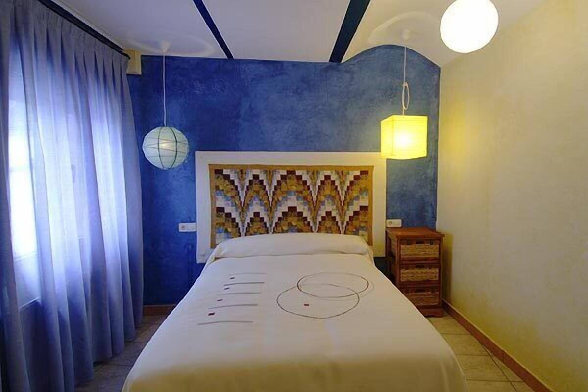 Ein Hotelzimmer mit Bett, Vorhängen, einer Wandlampe und einem Nachttisch.