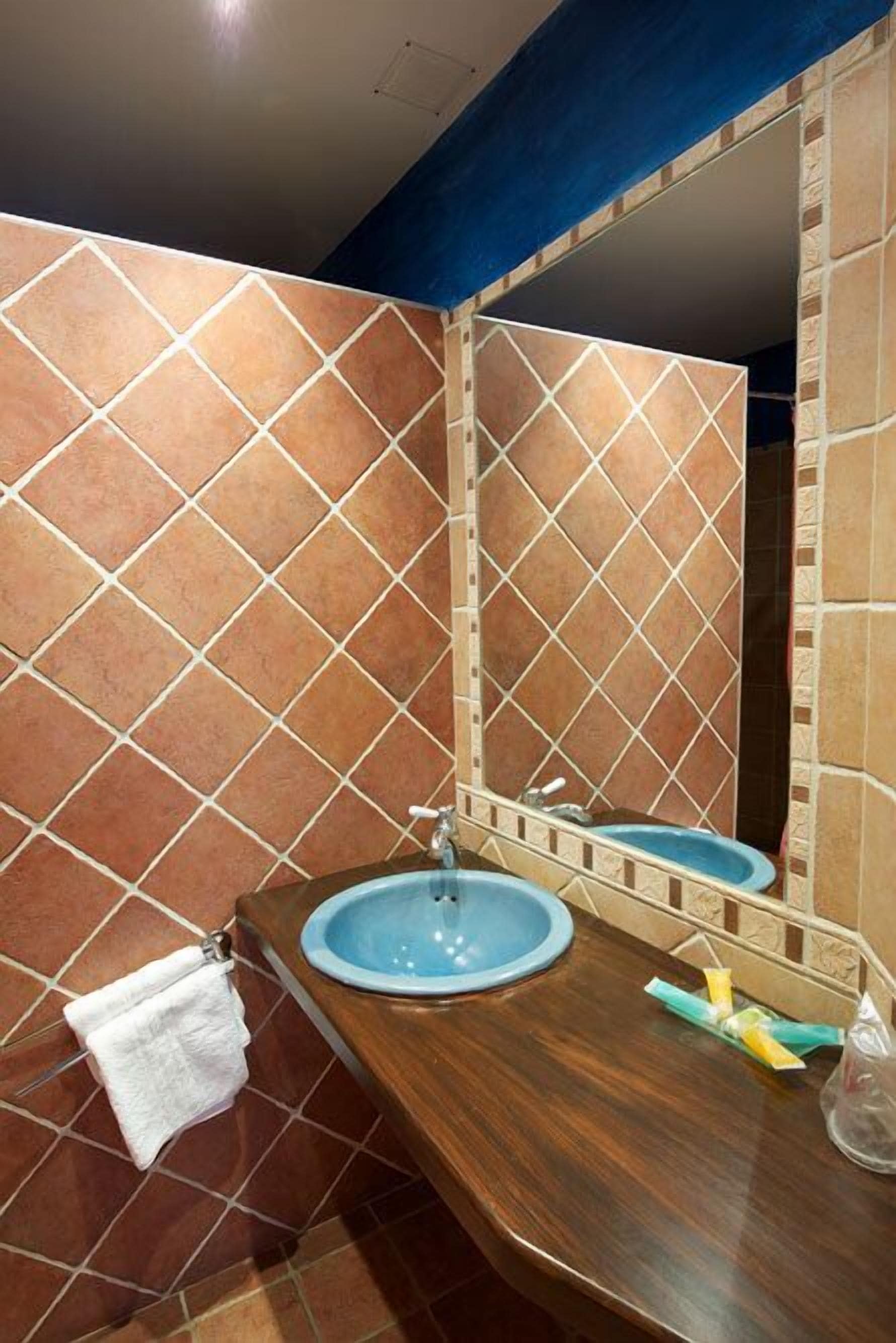 Un bagno con pareti piastrellate in marrone, un mobile vanitario in legno, un lavandino blu e un asciugamano bianco su un portasciugamani.