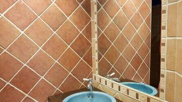 Un bagno con pareti piastrellate in marrone, un mobile vanitario in legno, un lavandino blu e un asciugamano bianco su un portasciugamani.