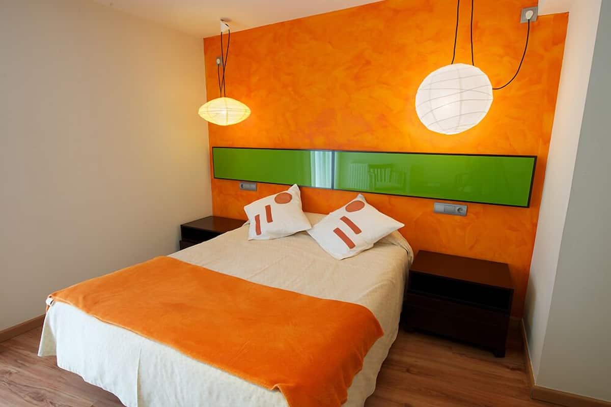 Ein modernes Hotelzimmer mit einem großen Bett, orangefarbener Bettwäsche, einem grünen Kopfteil und zwei Nachttischen.