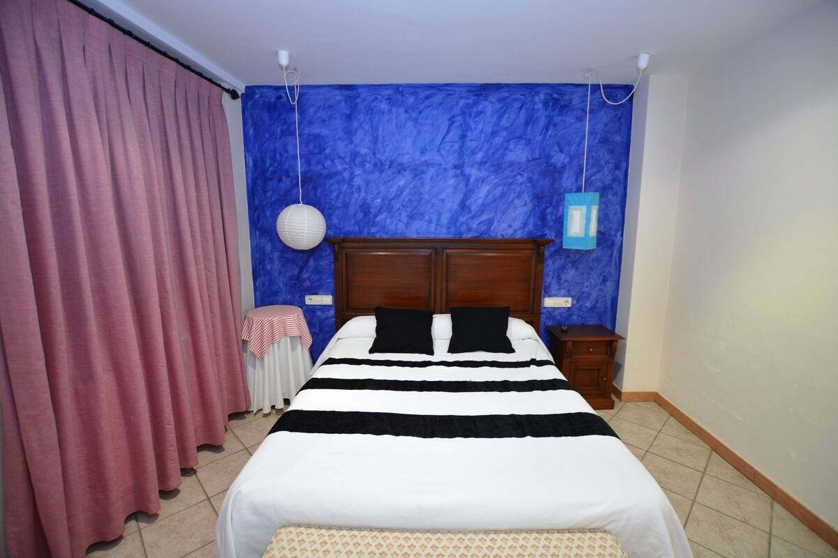 Ein Schlafzimmer mit Bett, Vorhängen, einem Nachttisch und einer Wandlampe.