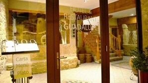 Entrada de un hotel con una escalera de madera, una recepción y un letrero que indica un restaurante.