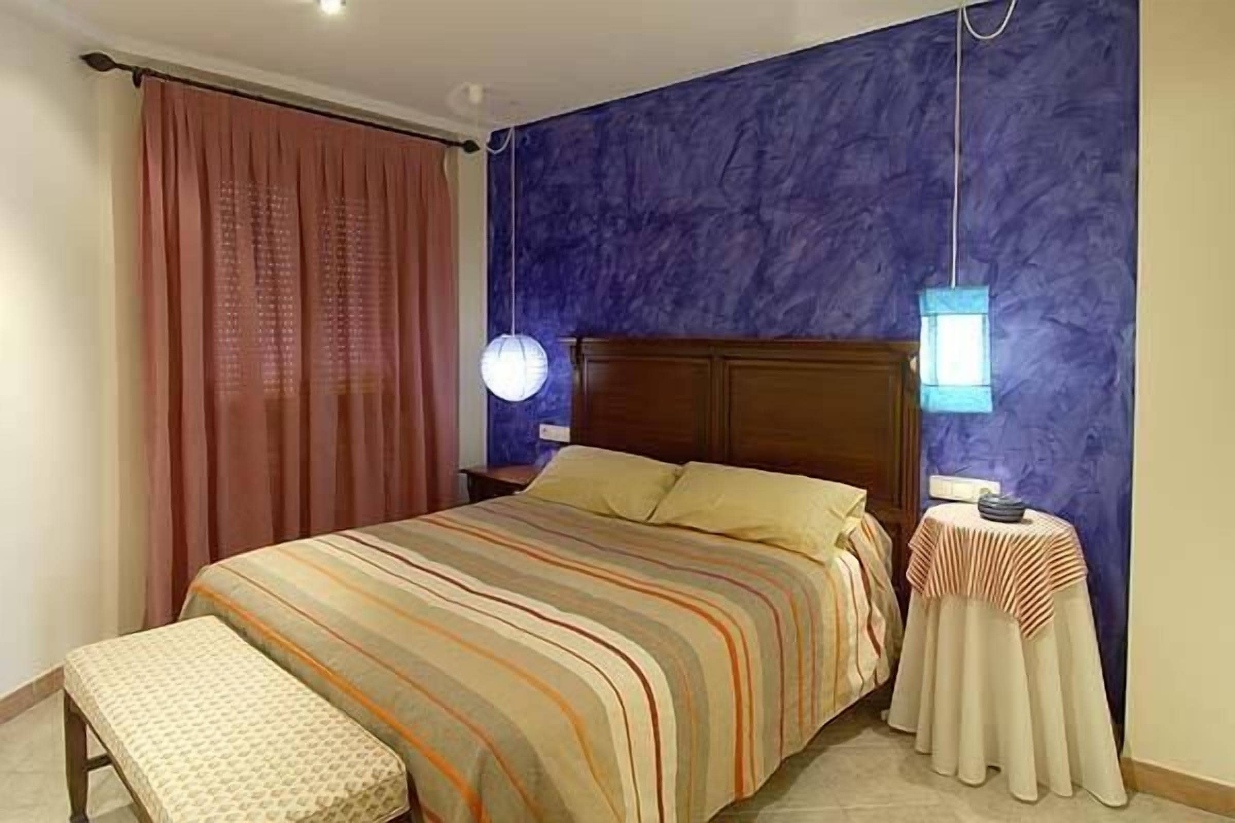 A bedroom with a bed, a bench, a nightstand, and a table with a lamp.