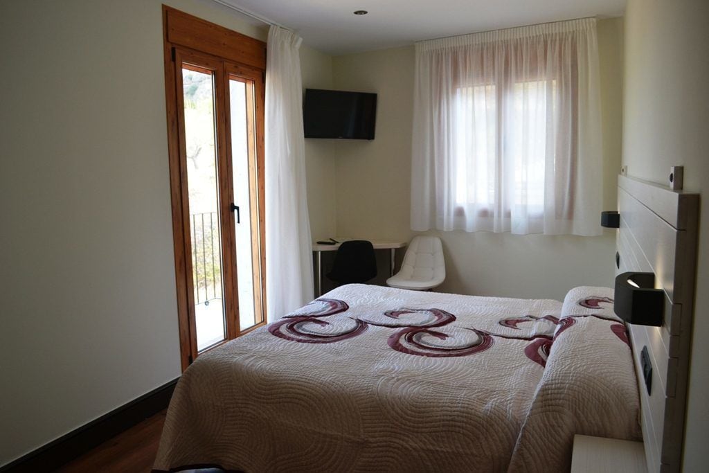 Une chambre à coucher avec un lit, un bureau, une chaise, une télévision et une fenêtre avec des rideaux.