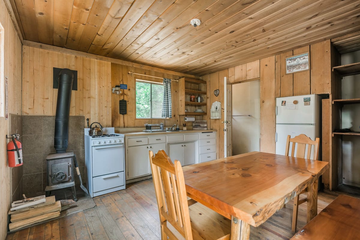 A wooden cabin interior with a kitchen, dining table, and a wood stove.
