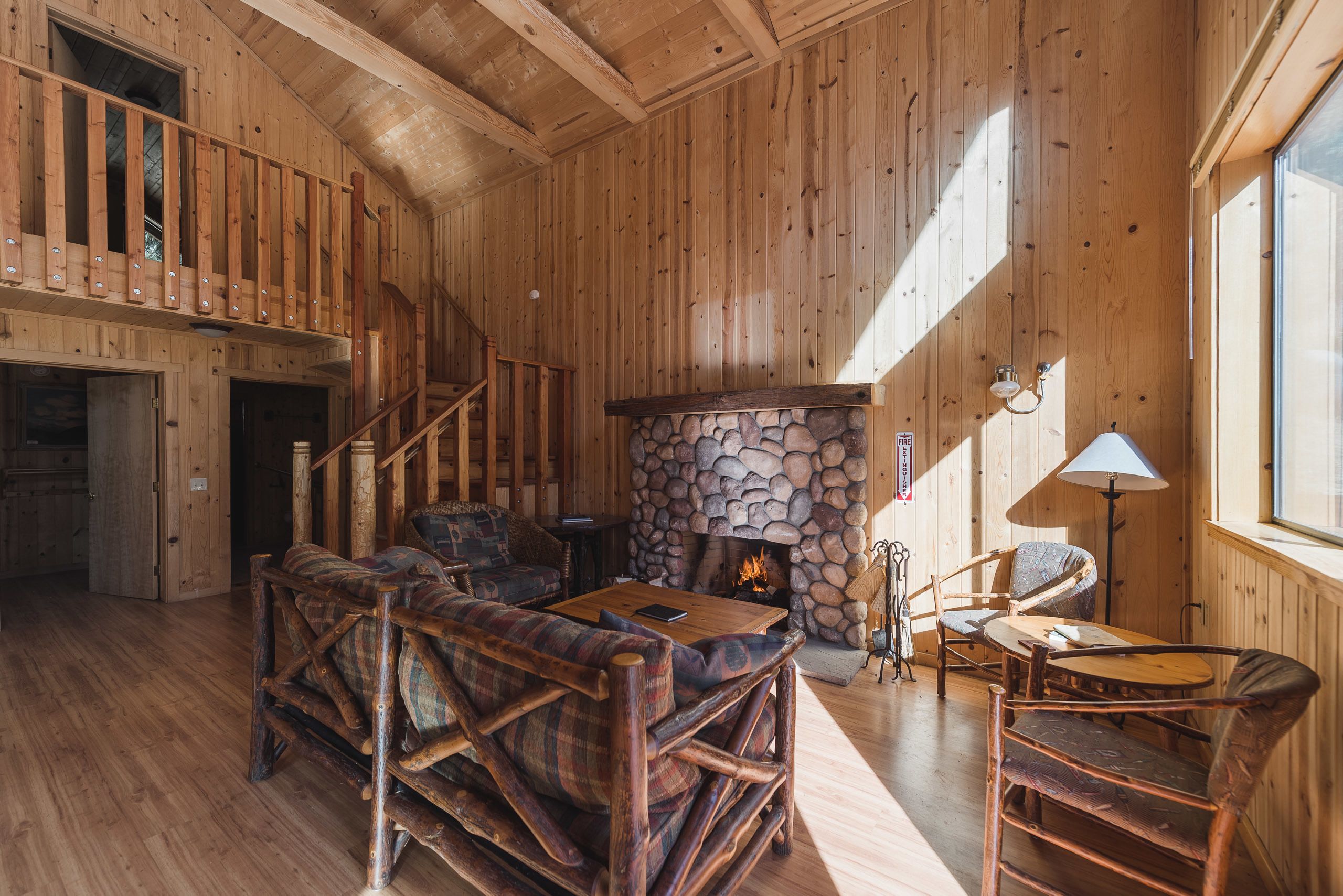 A wooden interior with a stone fireplace, a staircase, and a cozy seating area.