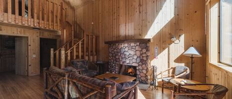 A wooden interior with a stone fireplace, a staircase, and a cozy seating area.