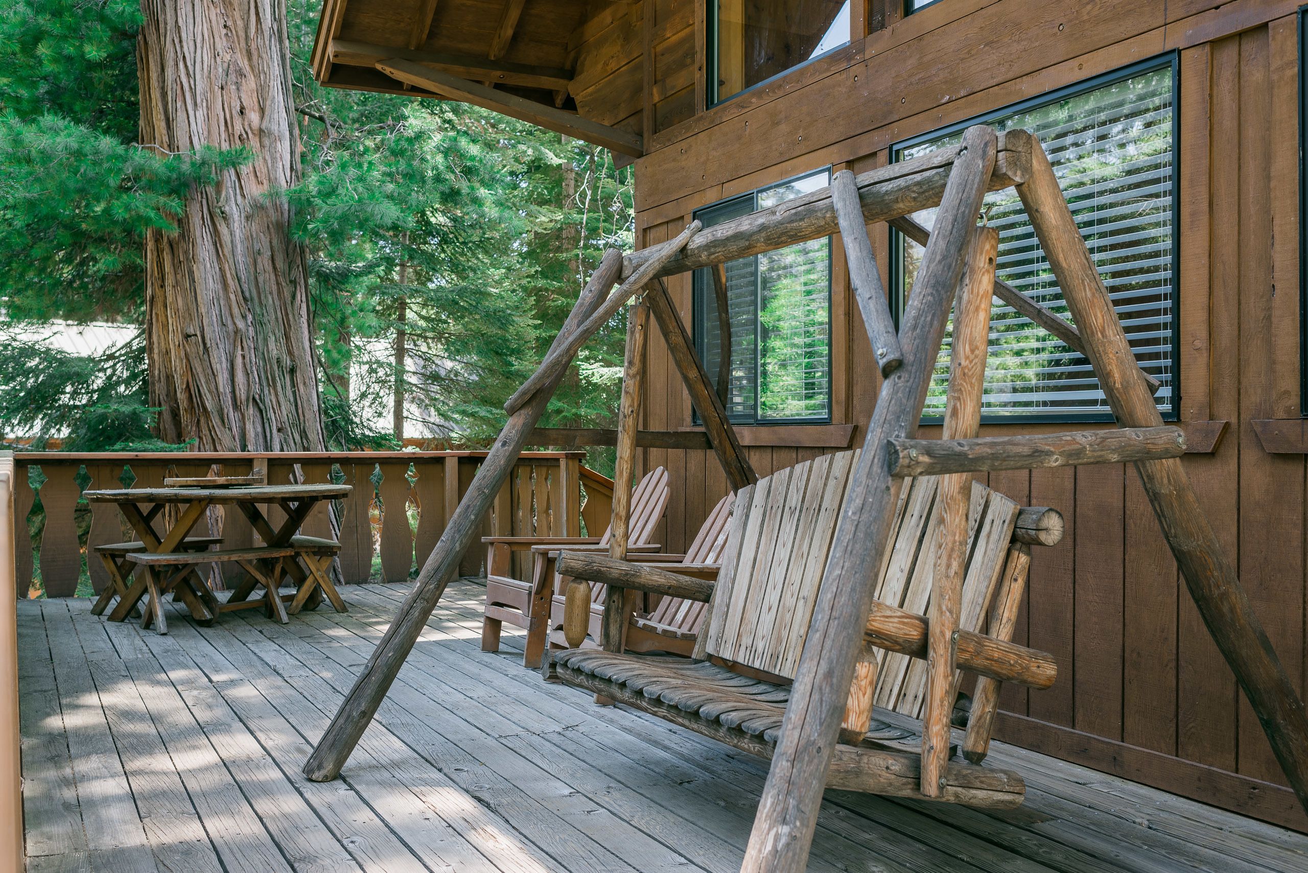 A wooden deck with a swing, picnic table, and Adirondack chairs.