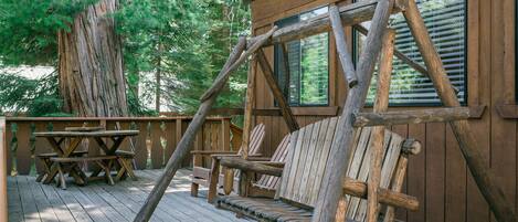 A wooden deck with a swing, picnic table, and Adirondack chairs.