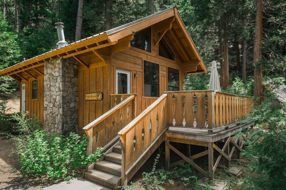 A wooden cabin with a stone foundation, wooden deck, and a staircase leading to the entrance.