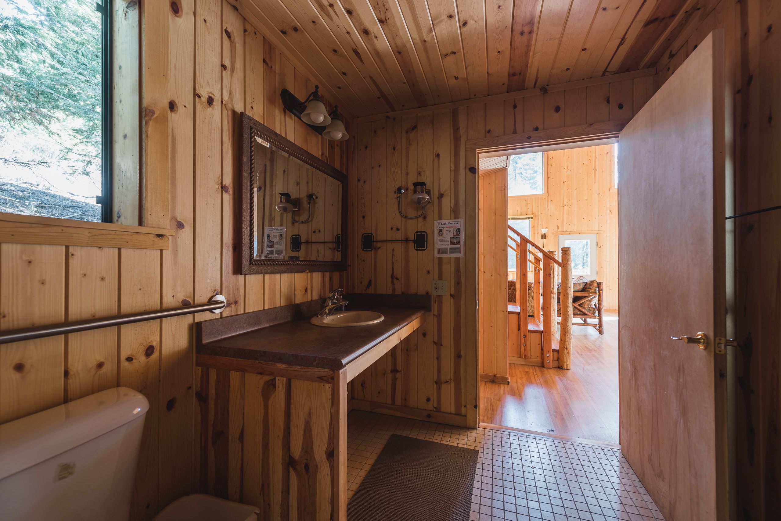 A wooden cabin bathroom with a sink, mirror, and toilet.