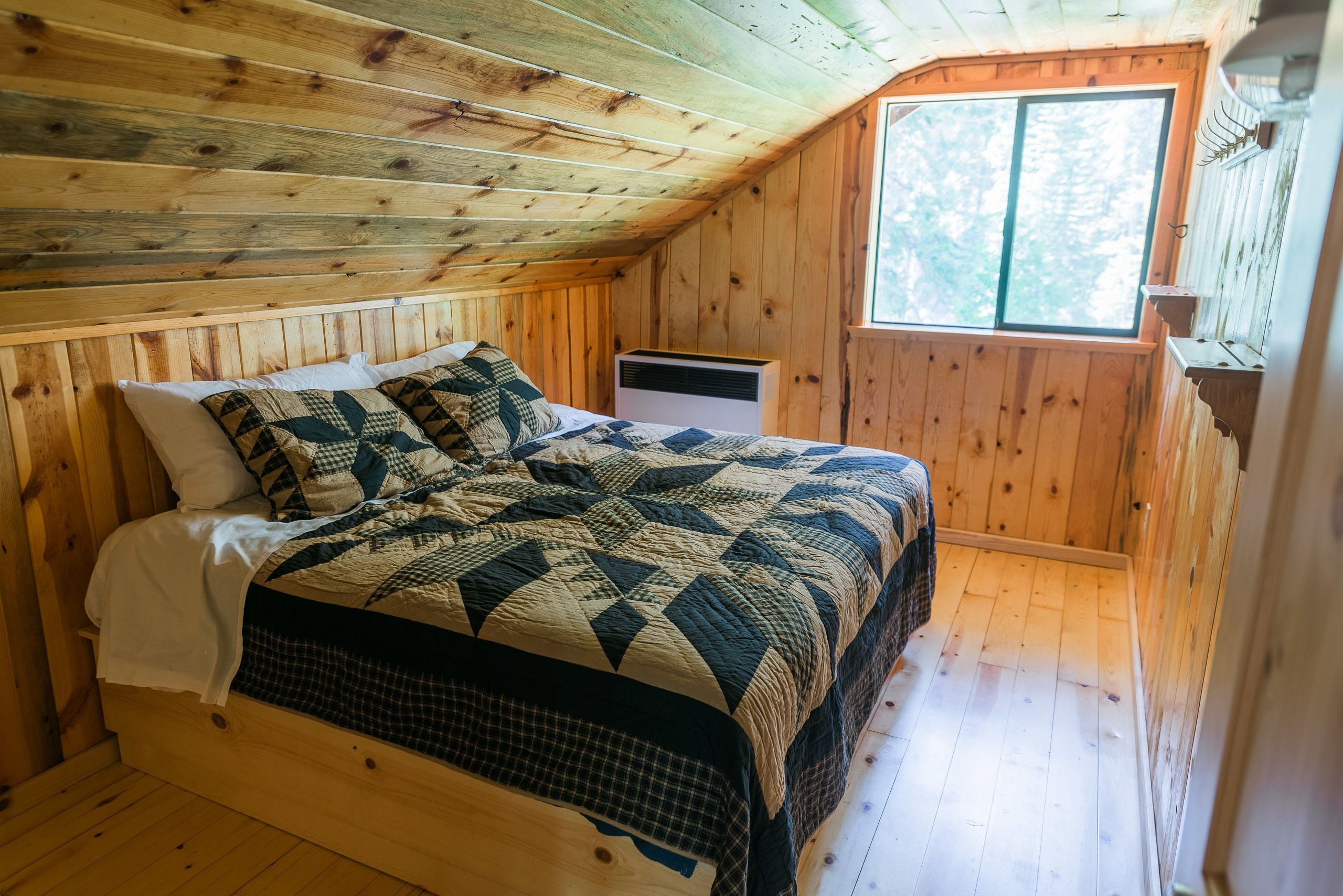 Une pièce aux murs lambrissés, avec un lit, une fenêtre et un radiateur encastré.