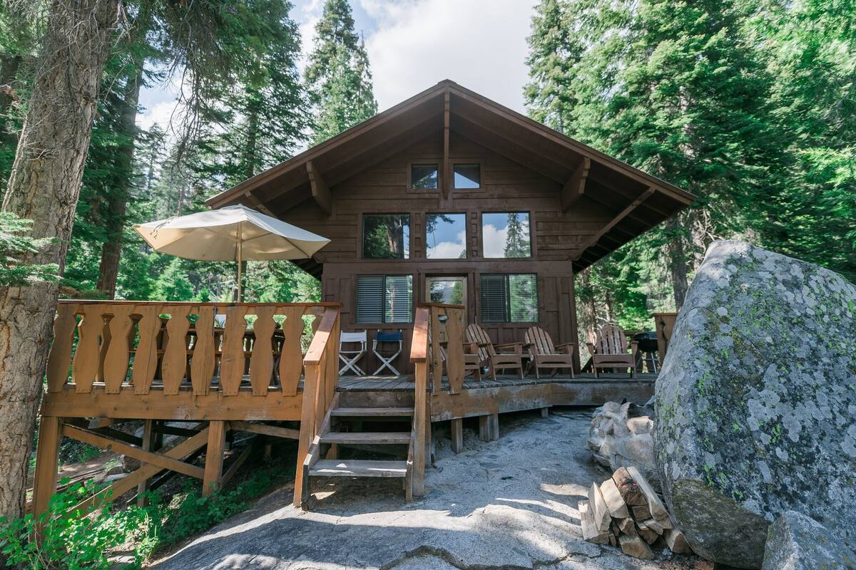 A wooden cabin with a deck, surrounded by trees.