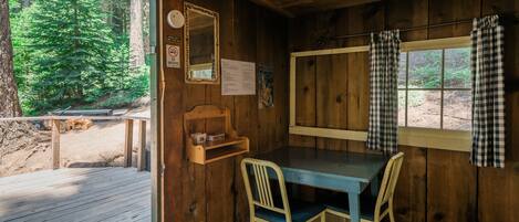 Una cabaña con interior de madera, una mesa con dos sillas, un espejo y una ventana con cortinas de cuadros.