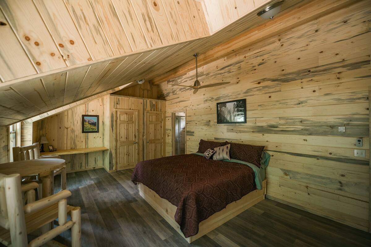 A wooden cabin bedroom with a bed, a desk, and a chair.