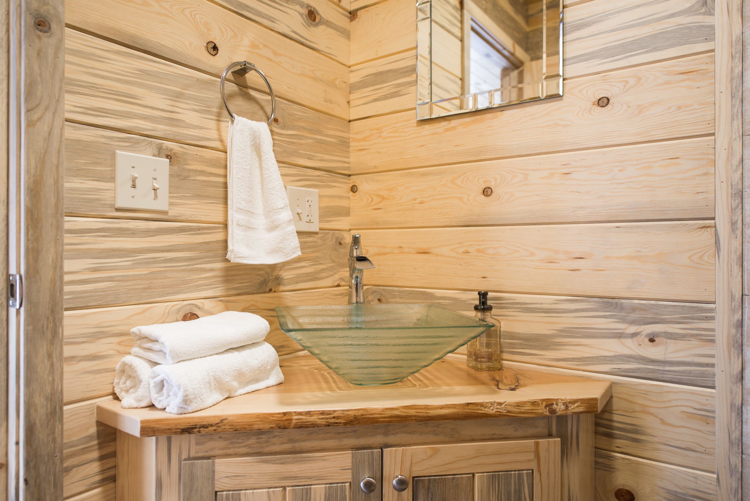 A wooden cabin bathroom with a glass sink, wooden cabinets, a towel rack, and a mirror.