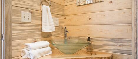 A wooden cabin bathroom with a glass sink, wooden cabinets, a towel rack, and a mirror.