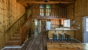 A wooden cabin interior with a central staircase, a kitchen area with a bar, and a dining space. - Silver City Mountain Resort (Three Rivers)