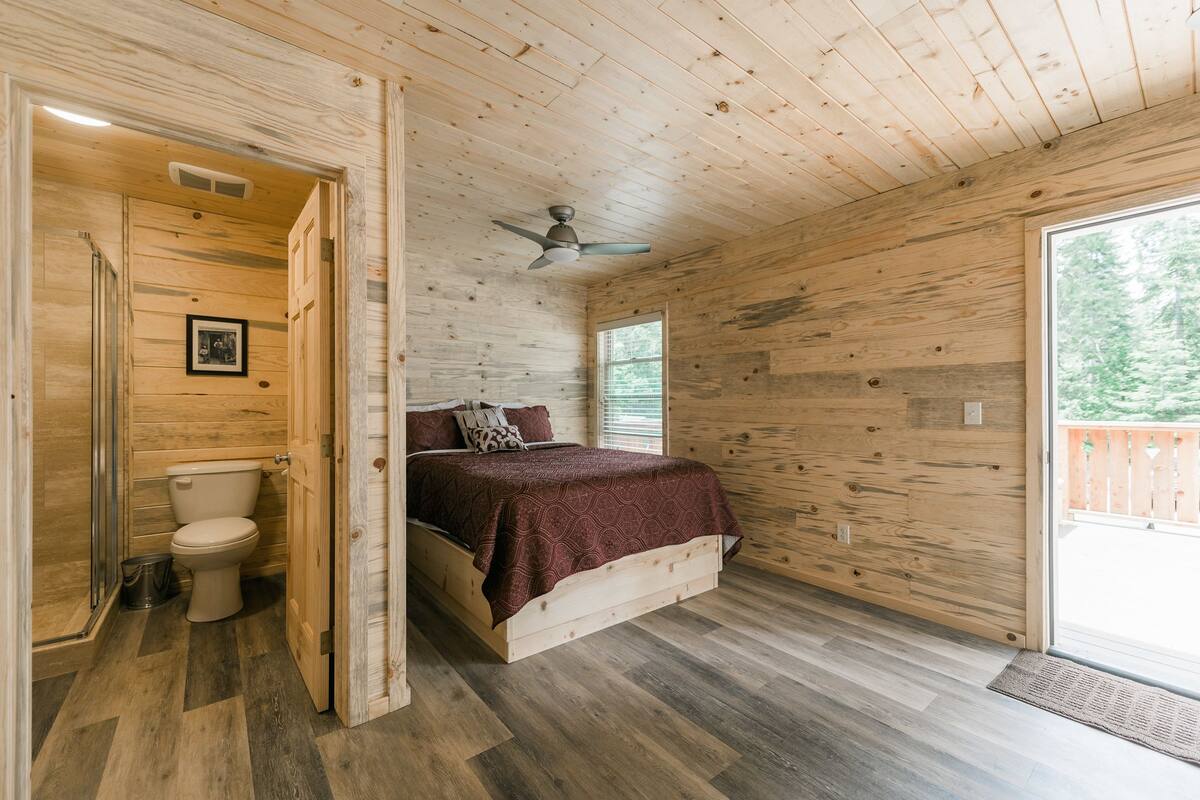 A wooden cabin bedroom with a bed, a ceiling fan, and a view of the outdoors.