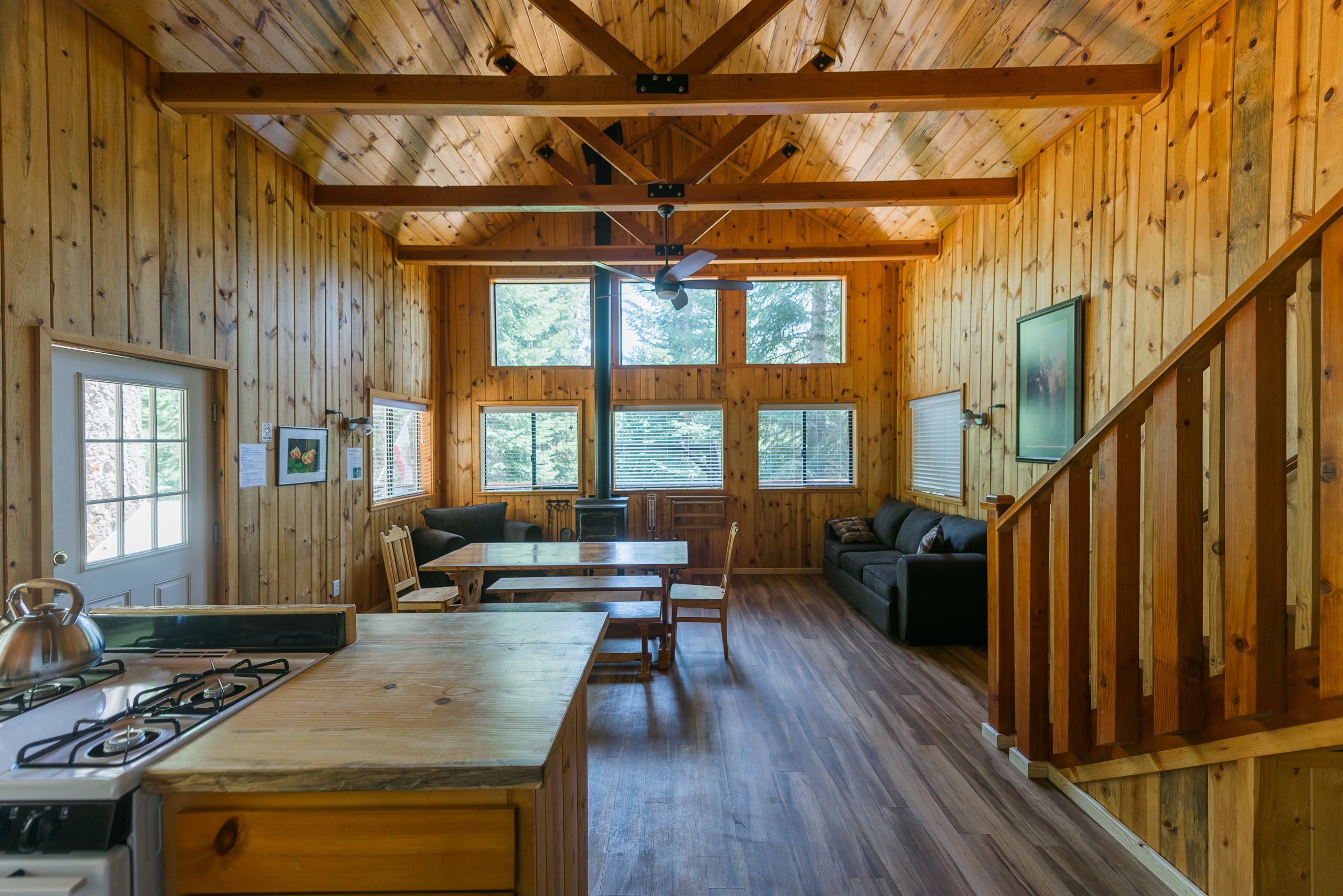 Interior de una cabaña con detalles de madera, un comedor, una cocina con estufa y una sala de estar con sofá y mesa.