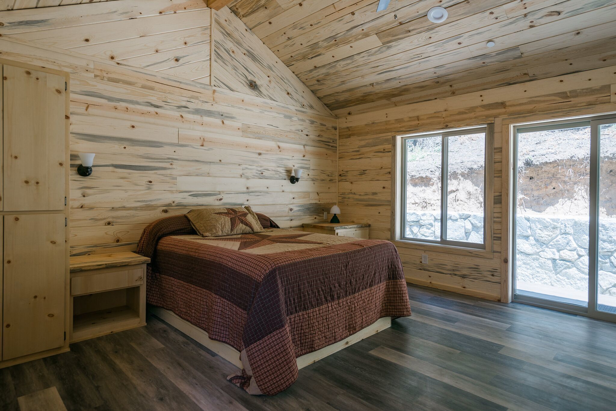 A wooden cabin bedroom with a bed, nightstands, and a window with a snowy view.