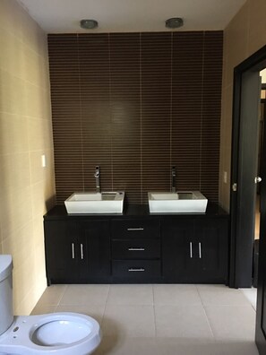 Un baño con dos lavamanos, un inodoro y muebles oscuros.
