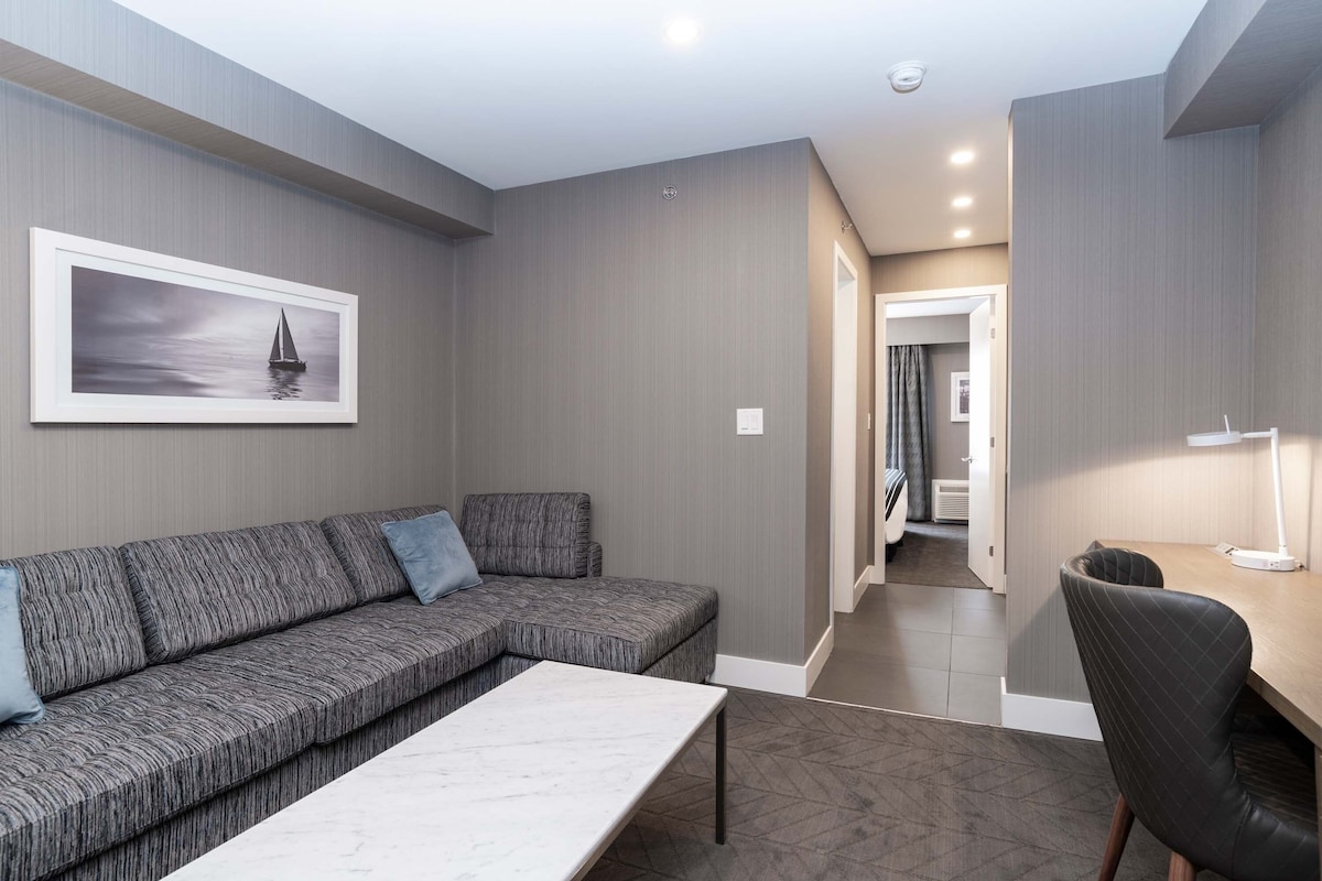 A modern living room with a grey sectional sofa, a white coffee table, and a framed picture of a sailboat on the wall.