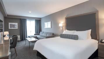 A modern hotel room with a large bed, a sofa, a desk, and a lamp.