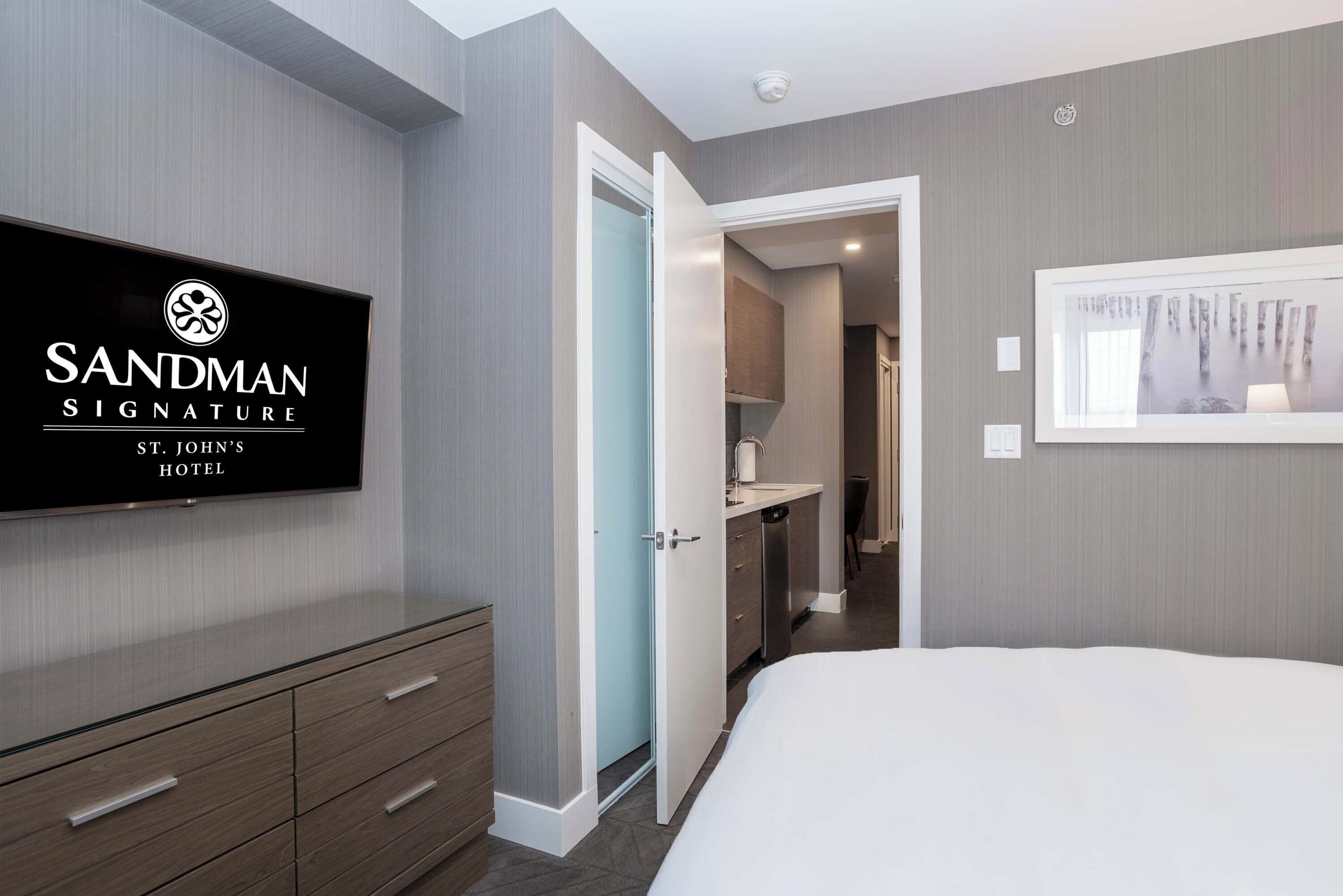 A hotel room with a bed, a TV on the wall, a wardrobe, and a bathroom visible through an open door.