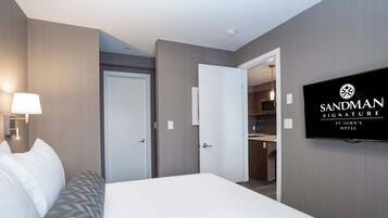 Una habitación de hotel con una cama, un televisor montado en la pared y una puerta que da a una cocina americana.