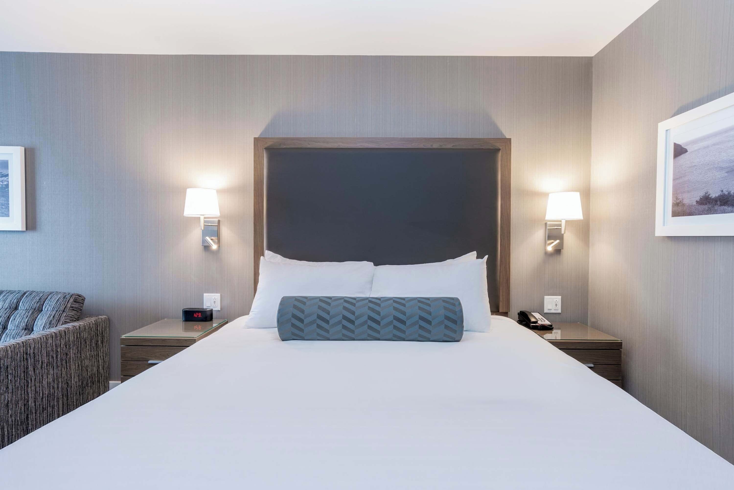 Une chambre d’hôtel avec un grand lit, deux tables de chevet, une chaise et une petite table avec une lampe.
