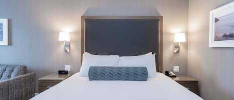 Une chambre d’hôtel avec un grand lit, deux tables de chevet, une chaise et une petite table avec une lampe.